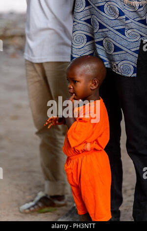 OUSSOUYE, SÉNÉGAL - Apr 30, 2017 : petit garçon sénégalais non identifiés en costume orange touche sa joue dans la forêt sacrée près de Kaguit village Banque D'Images