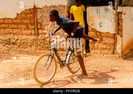 Route de BISSAU, GUINÉE B. - 1 mai 2017 : local non identifié, l'homme est assis sur le vélo dans un village en Guinée Bissau. Encore beaucoup de gens dans le pays li Banque D'Images