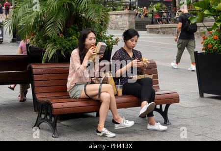 Deux jeunes femmes asiatiques assis sur un banc et manger des hamburgers à emporter dans la vieille ville de la Place Jacques-Cartier, Montréal, QC, Canada Banque D'Images