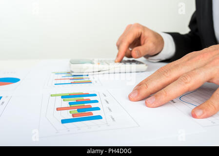 Vue rapprochée de la mains d'un homme d'analyse d'un graphique à barre a l'aide d'une calculatrice pour vérifier les statistiques et projections. Banque D'Images