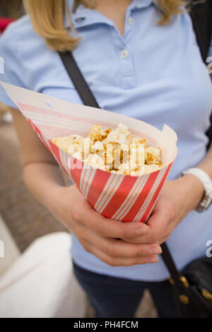 Femme blonde dans un tee-shirt bleu avec du papier à rayures sac plein de popcorn. Girl holding et manger du maïs soufflé sucré. Banque D'Images