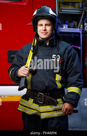 Photo de fireman wearing helmet with hammer contre fire engine Banque D'Images