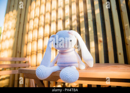 Un petit lapin blanc en tricot dans une robe rose sur la table en bois. Jouets en tricot, couture, fait main. Avec de longues oreilles de lapin mignon.En bunny. Décor de fête. Le jour de la Saint-Valentin. Tricotés à la main, toy Banque D'Images