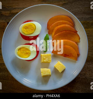 Tranches de pêches jaune sur plaque blanche avec un œuf dur, tomates et fromage sur fond bois vieilli - faible en glucides sains repas riche en protéines Banque D'Images