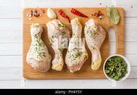 Les pilons de poulet dans la marinade avec la sauce, le poivre et les verts sur support en bois. Selective focus Banque D'Images