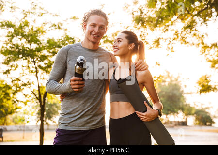 Photo de l'heureux couple aimant le sport fitness en plein air parc amis holding bouteille avec de l'eau et de remise en forme. Banque D'Images