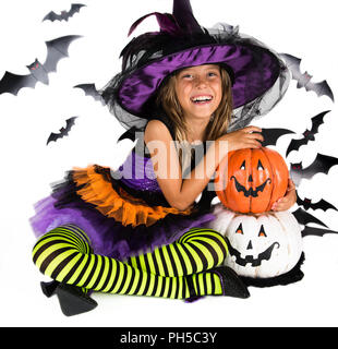 Happy Halloween sorcière & happy pumpkin. Petite fille avec un costume d'Halloween d'une sorcière avec chapeau, tenant deux jambes rayé smiley Halloween pumpkins Banque D'Images