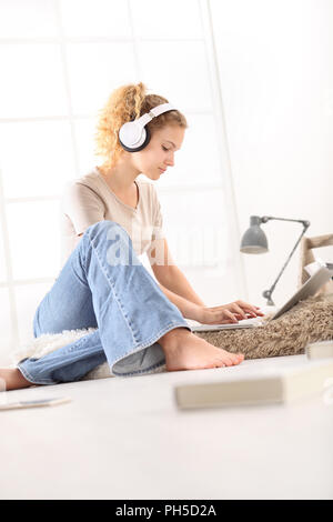 Woman with headphones assis sur le plancher dans la salle de séjour sur fenêtre blanche à l'arrière-plan Banque D'Images