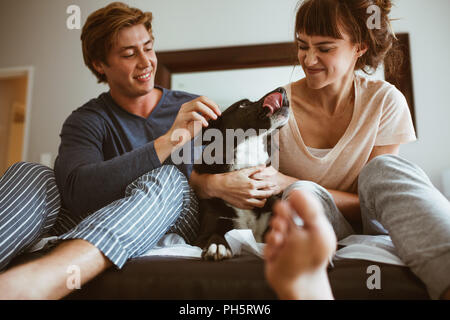 Couple cocooning un chien assis sur le lit à la maison. L'homme et la femme assis avec leur chien de compagnie sur lit et jouer avec elle. Banque D'Images