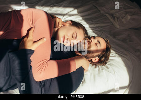 Man sur le bras de son mari avec la lumière du soleil entrant par la fenêtre. Couple relaxing on bed holding les uns les autres avec les yeux fermés. Banque D'Images