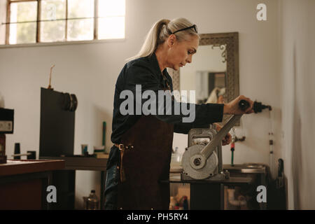 Femme mature goldsmith ouvrant metal sur l'artisanat. Senior female using traditional metal rolling machine en atelier de joaillerie. Banque D'Images