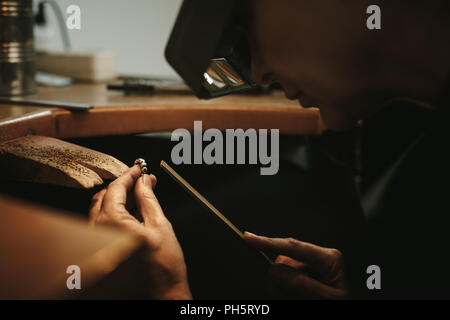 Gros plan d'une femme de l'orfèvre et façonnant un anneau non fini avec un outil au poste de travail en atelier. Fabricant de bijoux mature portant magnifying gl Banque D'Images