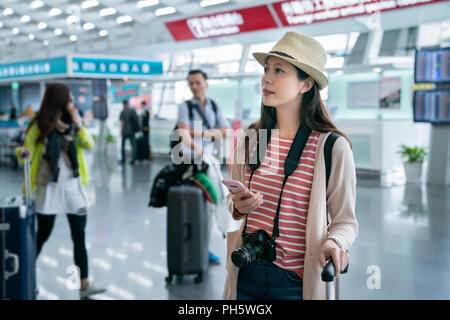 Contrôle des visiteurs quelque chose en attendant. holding smartphone à la main. par l'arrière-plan de boutiques dans l'aéroport. Banque D'Images