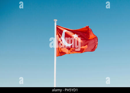 Un drapeau turc sur un mât contre un ciel bleu. Banque D'Images