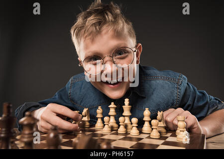 Smiling little boy in lunettes jouant aux échecs isolé sur fond gris Banque D'Images