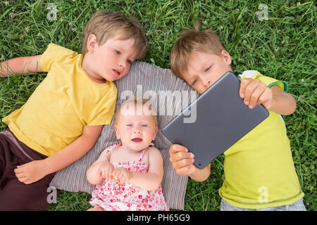 Les enfants occupent l'ipad dans leurs mains allongés sur l'herbe. Banque D'Images