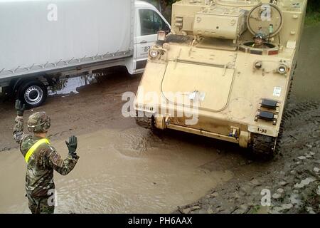 Un soldat du 2e Bataillon, 5e régiment de cavalerie, 1st Armored Brigade Combat Team, 1re Division de cavalerie guides un pilote pendant les opérations de chargement ferroviaire la gare d'Sendreni en Roumanie dans le cadre de détermination de l'Atlantique, un exercice d'entraînement durables entre l'OTAN et les forces américaines, le 27 juin 2018. Les soldats chargés de divers véhicules blindés dont plusieurs M2A3 Bradley de combat, plusieurs M88A2 Hercules armored de dépannage et des dizaines de véhicules à roues pour de futures missions d'entraînement à Galati, Roumanie Zone de formation. Banque D'Images