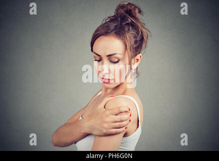 Jeune brunette se frottant l'épaule La douleur commune et d'avoir dans l'article sur fond gris Banque D'Images