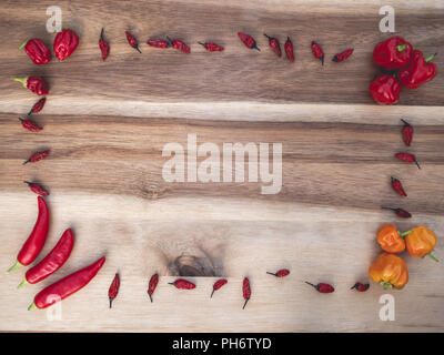Cadre de différents types de piments rouges et orange sur une planche en bois Banque D'Images