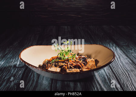 Nouilles soba au tofu et légumes décorées de graines germées de tournesol sur plaque sur table en bois Banque D'Images