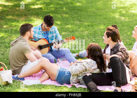 Les amis à jouer de la guitare à pique-nique au parc d'été Banque D'Images