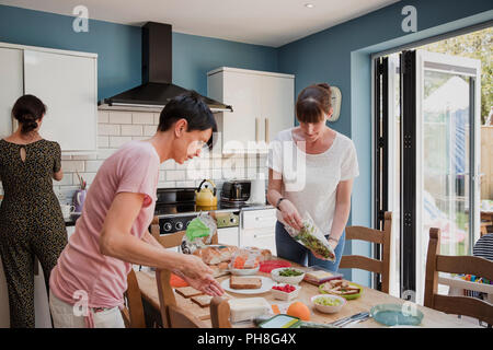 Thre woman standing in la autour d'une table à manger possèdent. Les femmes æ préparer la nourriture pour le déjeuner. Quelques Preping et salade sandwiches. Banque D'Images