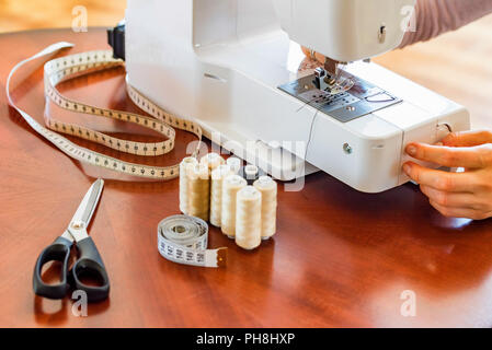 Couturier ou couturière travaille à l'aide de la machine à coudre. Bobines, ciseaux, ruban de mesure et d'une machine à coudre. Lieu de travail Banque D'Images