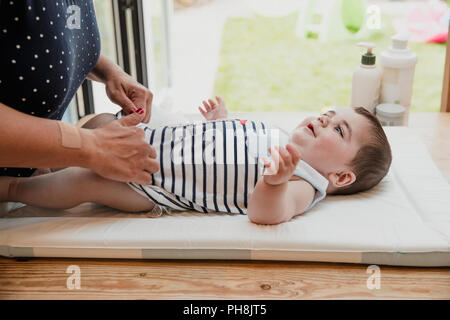 Vue latérale d'un petit garçon allongé sur le dos. Le petit garçon prend ses nappy changé par sa mère qui est méconnaissable. Banque D'Images