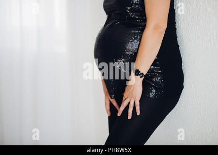 Femme enceinte en noir haut mousseux ventre embrassant sur fond blanc. Banque D'Images