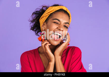 Portrait of a smiling young African woman in headband debout sur fond violet, sticking tongue out Banque D'Images