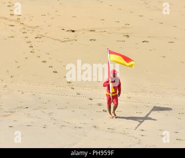 Sauveteur RNLI sur devoir transporter un pavillon rouge et jaune en face de la plage,Riviere Towans beach, Phillack, Hayle cornwall,Angleterre,,UK Banque D'Images