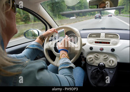 BOTTROP, ALLEMAGNE - Aug 16, 2018 : une femme blonde est sa lecture sur son smartphone whatsApp tandis qu'elle est conduite sur une route à pleine vitesse. Banque D'Images
