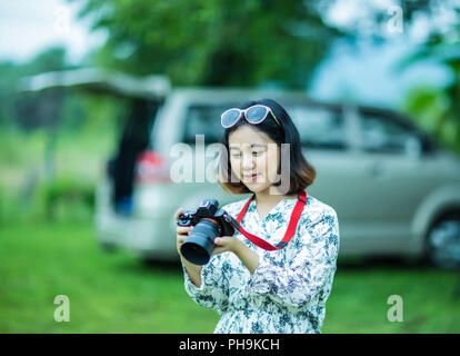 Happy asian girl holding et la vérification de l'appareil photo dans le parc Banque D'Images