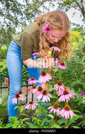 Young caucasian woman smelling fleur d'échinacée dans jardin Banque D'Images