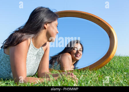 Femme couchée sur l'herbe à l'extérieur à la recherche dans le miroir Banque D'Images