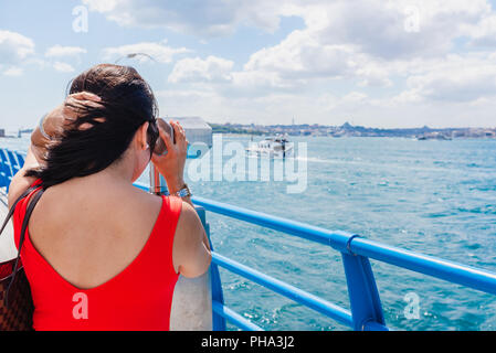 Belle femme chinoise regarde à travers des jumelles touristiques sur Bosphore,une destination populaire à Istanbul, Turquie Banque D'Images