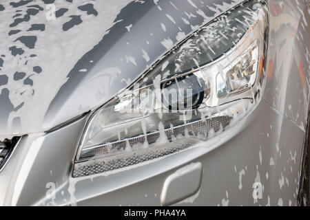 Un gros plan de mousse de savon sur le côté droit de la lumière principale d'une voiture d'argent Banque D'Images