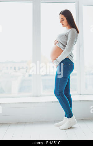 Expecting woman holding her baby bump debout dans la salle de séjour Banque D'Images