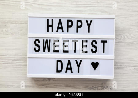 Conseil moderne avec texte 'Happy Sweetest Day' mot over white surface en bois, vue du dessus. À partir de ci-dessus, mise à plat, les frais généraux. Banque D'Images