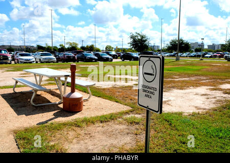 Espace fumeurs affiche à l'extérieur avec banc, élimination de cigarette, prise et parking en arrière-plan. Banque D'Images