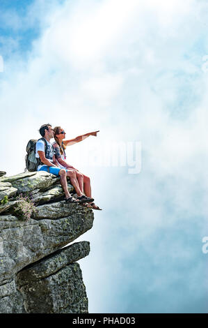 Travel concept : les jeunes touristes couple avec sacs à dos assise sur le bord d'une falaise avec approche de puffy white cloud. Copier l'espace. Banque D'Images