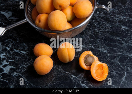 Organique mûres les abricots dans une passoire en acier. Composition dans un style rustique - jaune bio abricots juteux dans son ensemble et passoire en acier et des moitiés d'abricots o Banque D'Images