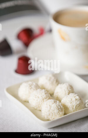 Close-up of white des bonbons balle sain avec une tasse et des capsules à café sur la table. Petit-déjeuner sucré ou un en-cas. Pause café. Noix de coco brut candi Banque D'Images