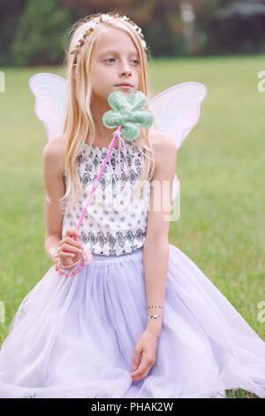 Portrait of smiling blonde blanc caucasien enfant kid girl with long hair wearing pink fairy wings et tutu jupe en tulle holding baguette magique, heureux les natures mortes Banque D'Images