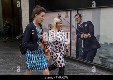 Les femmes passent devant une affiche présentant un homme d'affaires bénéficiant de temps libre sur le cours de golf portant un costume bleu - a favorisé le style et la couleur de l'homme dans la ville de Londres, le quartier financier de la capitale - aka le Square Mile, le 29 août 2018, à Londres, en Angleterre. Banque D'Images