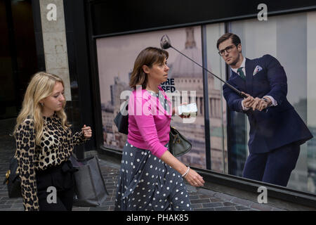 Les femmes passent devant une affiche présentant un homme d'affaires bénéficiant de temps libre sur le cours de golf portant un costume bleu - a favorisé le style et la couleur de l'homme dans la ville de Londres, le quartier financier de la capitale - aka le Square Mile, le 29 août 2018, à Londres, en Angleterre. Banque D'Images