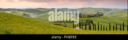 Vue panoramique de coucher de soleil sur l'Agriturismo Baccoleno et sentier sinueux avec des cyprès, Asciano en Toscane, Italie, Europe Banque D'Images