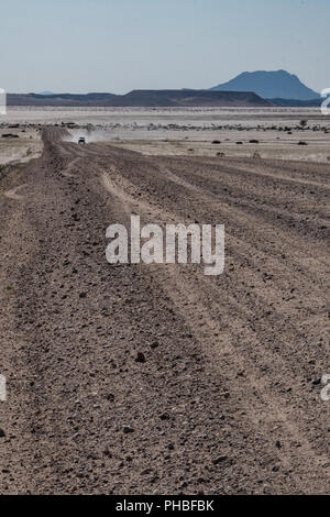 Quatre par quatre dans le véhicule sur une distance longue ligne droite de gravier, les montagnes bleues à l'arrière-plan, au nord de la Namibie, l'Afrique, de Solitaire Banque D'Images