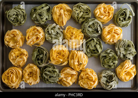 Le séchage des pâtes fraîches maison pâtes sur une plaque de cuisson avec des boules de séchée et ruban vert vue d'au-dessus des nouilles dans une vie encore laïcs Banque D'Images