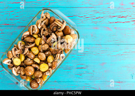 Cocotte en verre avec des dés de pommes de terre et champignons bella bébé prêt à être rôti au four sur un fond de bois peinture craquelé bleu avec l'exemplaire Banque D'Images